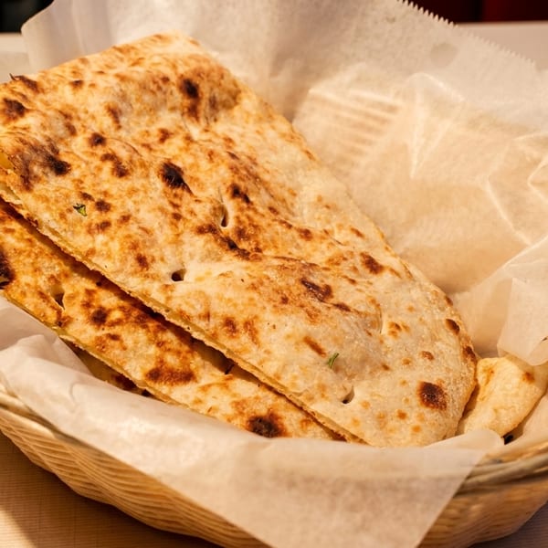 A woven basket lined with parchment paper holds several pieces of golden-brown naan bread.