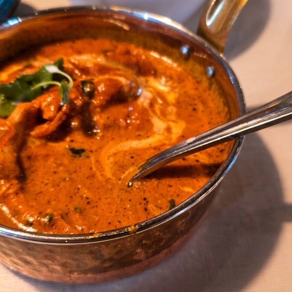 A copper pot filled with creamy orange curry, garnished with cilantro, and a spoon resting inside.