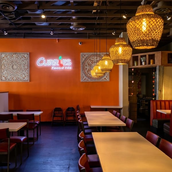 Interior of Curries restaurant with orange and green walls, tables, red chairs, and booth seating.