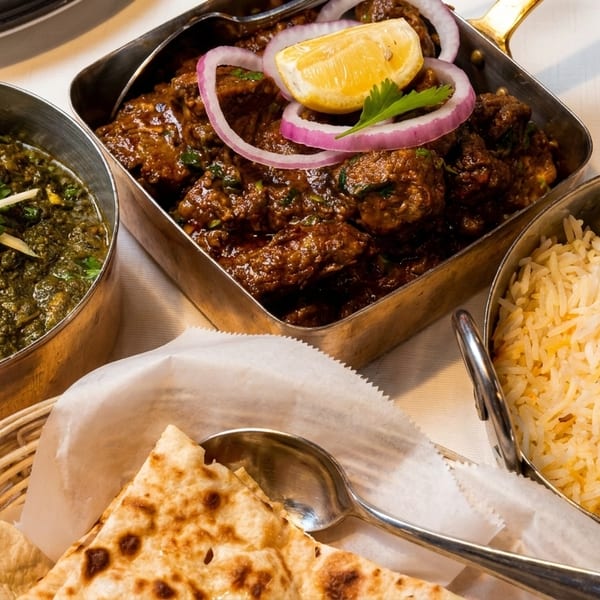 Indian meal with palak paneer, lamb curry, basmati rice, and naan bread on a white tablecloth.