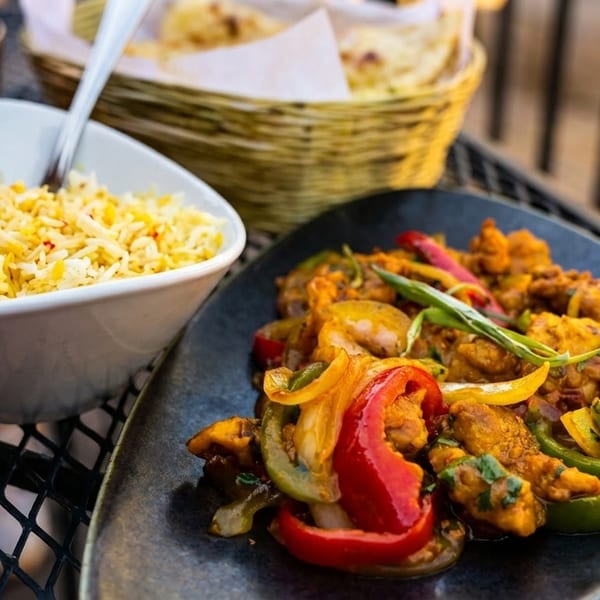 Indian dish with chicken, bell peppers, and onions, served with a side of yellow rice.