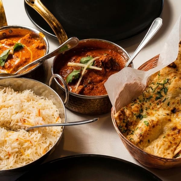 Indian meal with two curries, basmati rice, and naan bread in a basket.