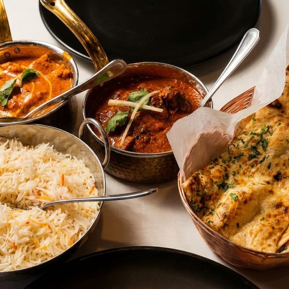 Indian meal with two curries, basmati rice, and naan bread in a basket.