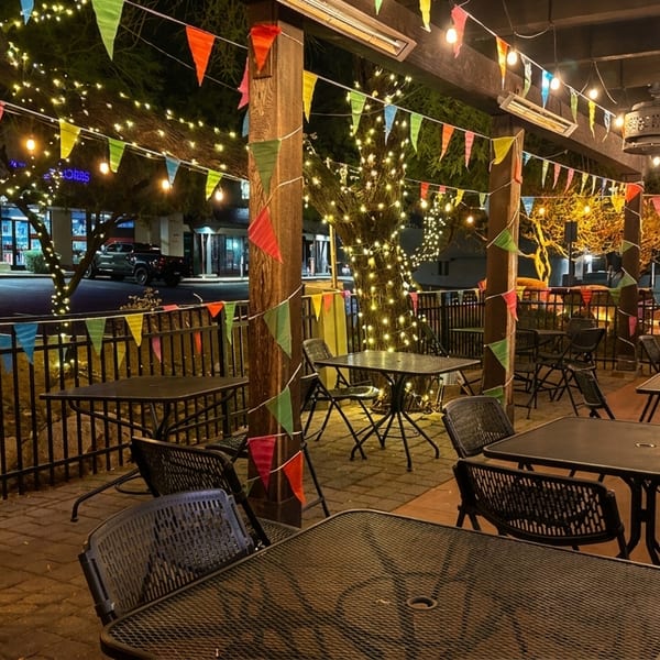 Outdoor patio at night with strung lights, colorful pennants, and empty tables and chairs.